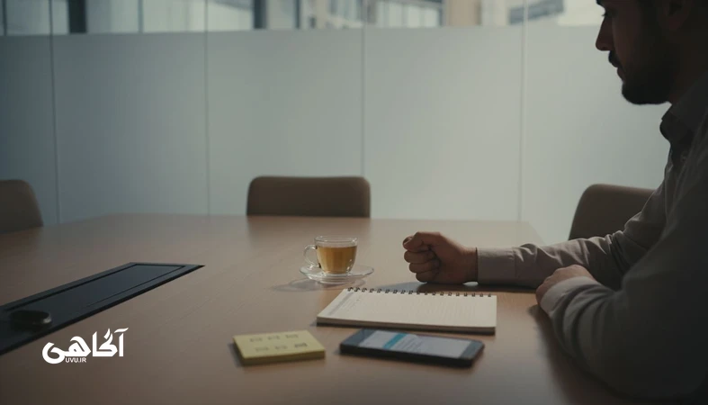 تصویر مفهومی از فرار از گفتگوهای دشوار در محیط کار برای مجله آگاهی؛ دست روی میز کنار گوشی با پیام ارسال‌نشده و فضای جلسه آرام